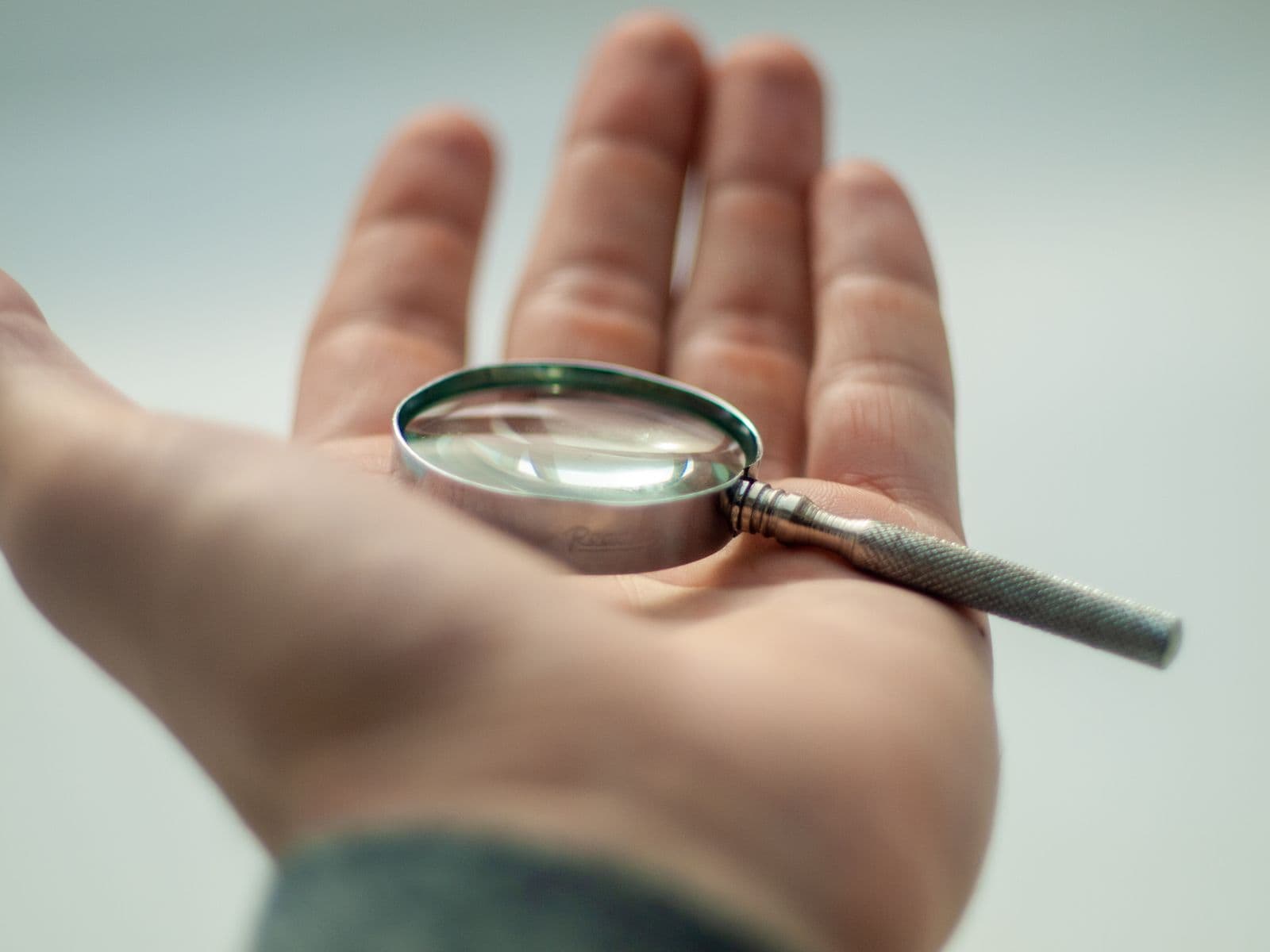 A hand holding a magnifying glass, symbolizing close inspection.