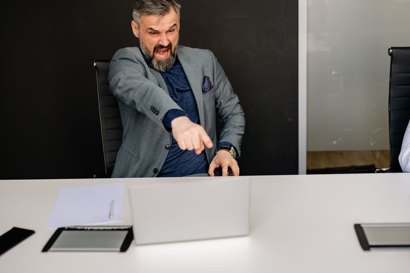 A businessman gesturing in frustration at a laptop screen in an office.
